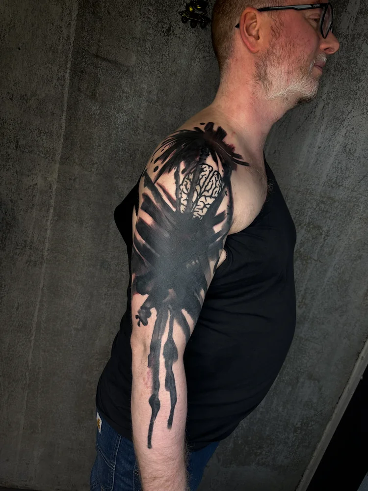 Abstraktes Blackout-Tattoo am Arm mit breiten schwarzen Formen und langen fließenden Linien