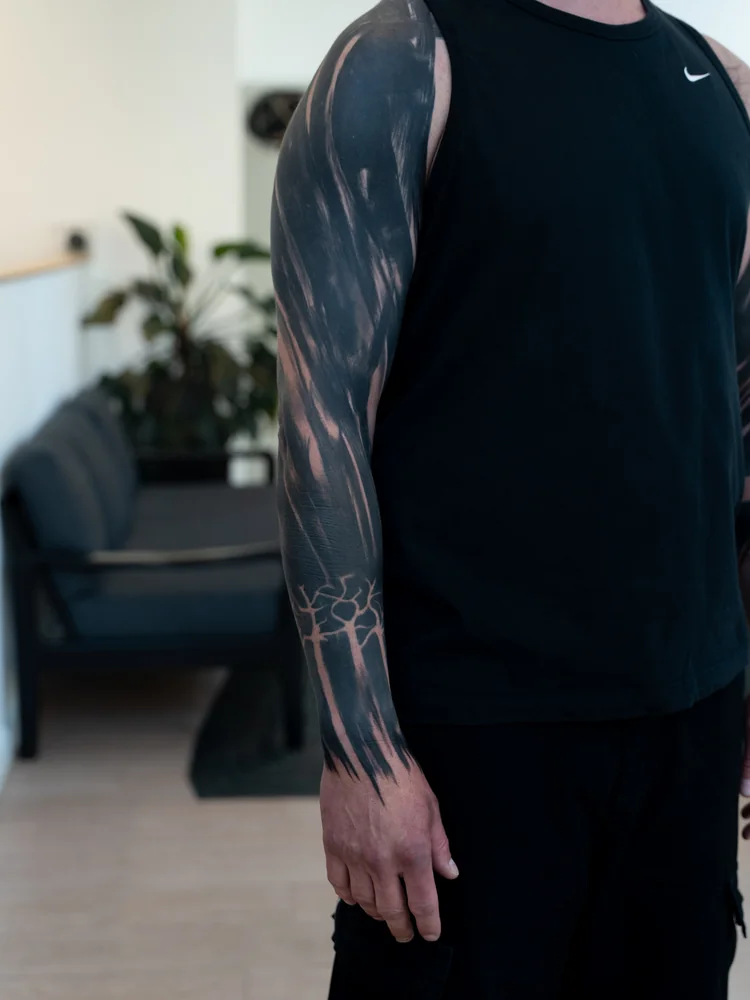 Abgeheilt: Abstraktes Blackout-Tattoo am Arm mit fließenden schwarzen Flächen und schmalen Hautlinien
