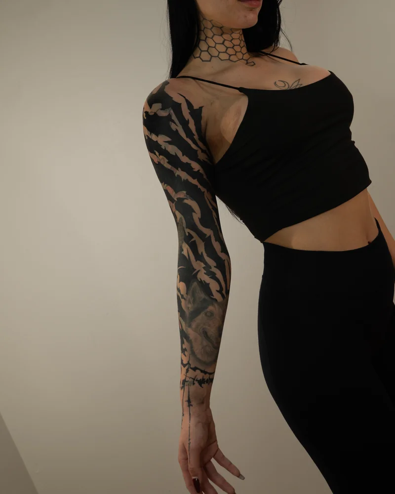 Blackout-Armtattoo mit fließenden schwarzen Formen und offenen Hautflächen um bestehende Motive