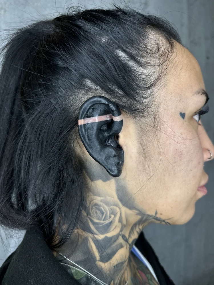 Blackout-Tattoo am Ohr mit einem schmalen freien Hautband