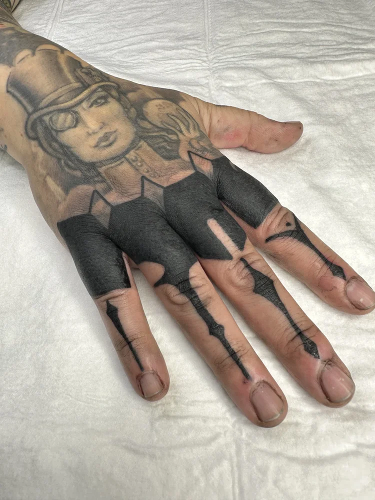 Blackout-Tattoo an Hand und Fingern mit schwarzen Flächen und geometrischen Linien unter einem bestehenden Porträtmotiv