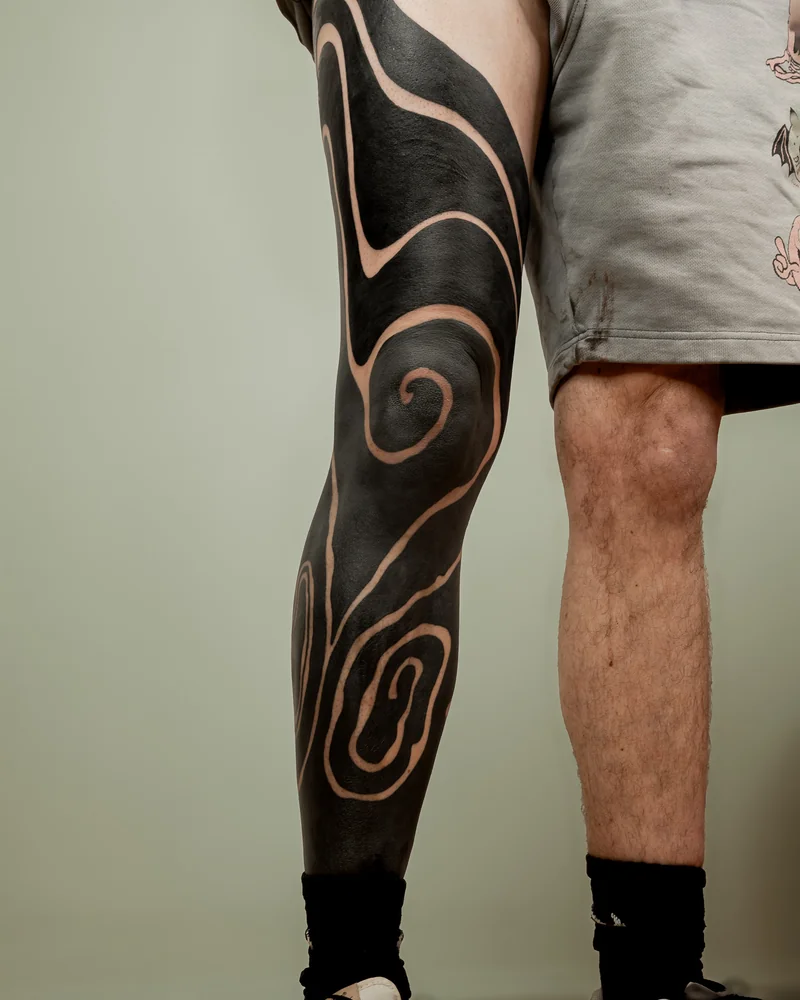Blackout-Tattoo am Bein mit geschwungenen Linien aus freier Haut