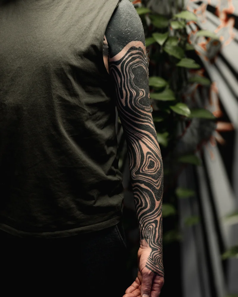 Abgeheilt: Fließende Blackwork-Linien am Arm mit ineinander verschlungenen schwarzen Bändern