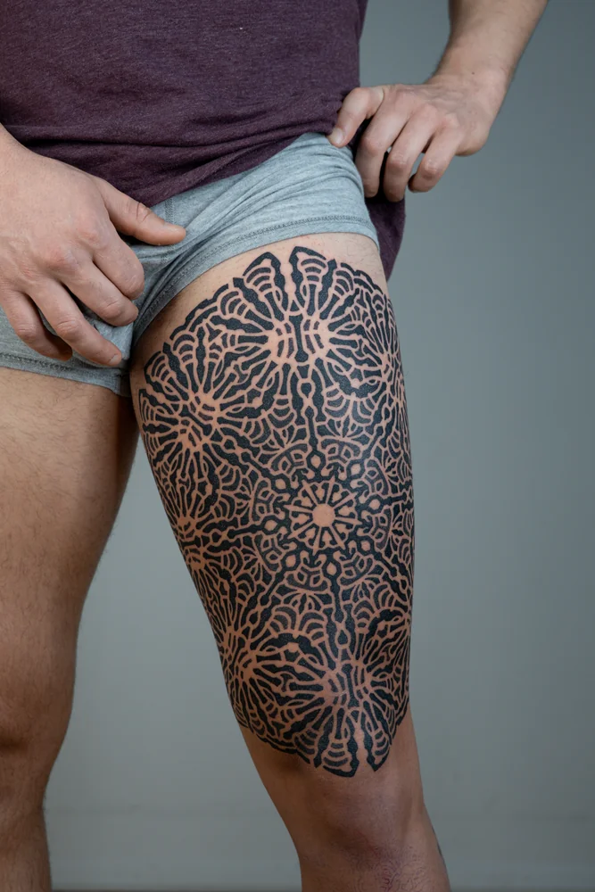 Dotwork-Tattoo am Oberschenkel mit wiederholten floralen Mandalas