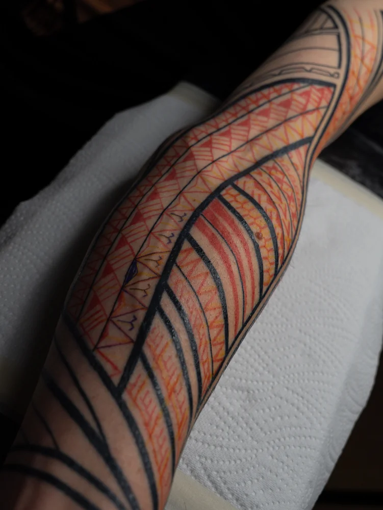 Freehand-Entwurf am Arm mit roten, gelben und violetten Musterlinien zwischen schwarzen Tattoo-Linien