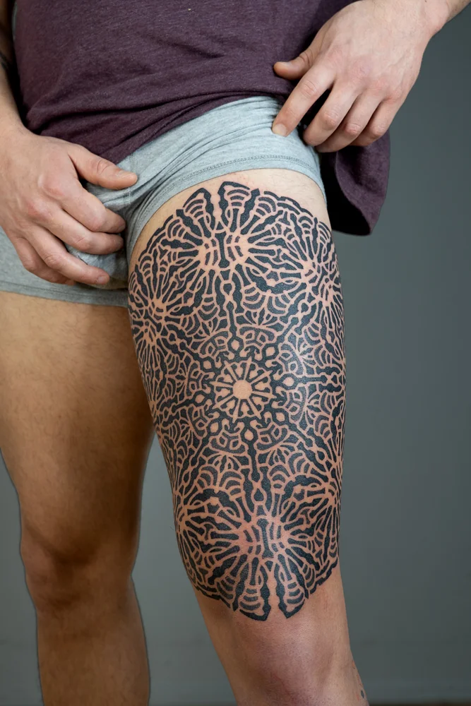 Großflächiges geometrisches Mandala-Tattoo am Oberschenkel mit schwarzen Linien und wiederholten Rundmustern