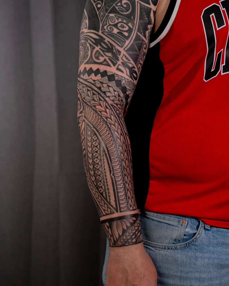 Geometrischer Tribal-Sleeve mit maskenartigen Motiven und gemusterten Bändern