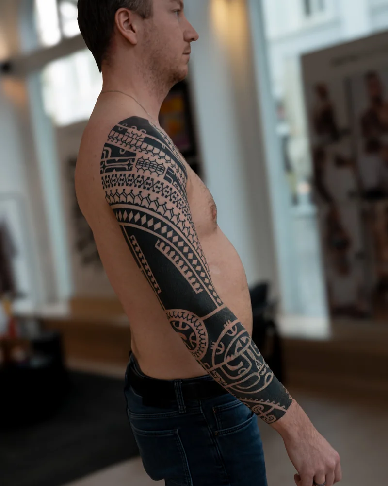 Abgeheiltes Cover-up am Arm mit schwarzen Musterbändern und weißer Tinte, um das alte Tribal optisch abzumildern