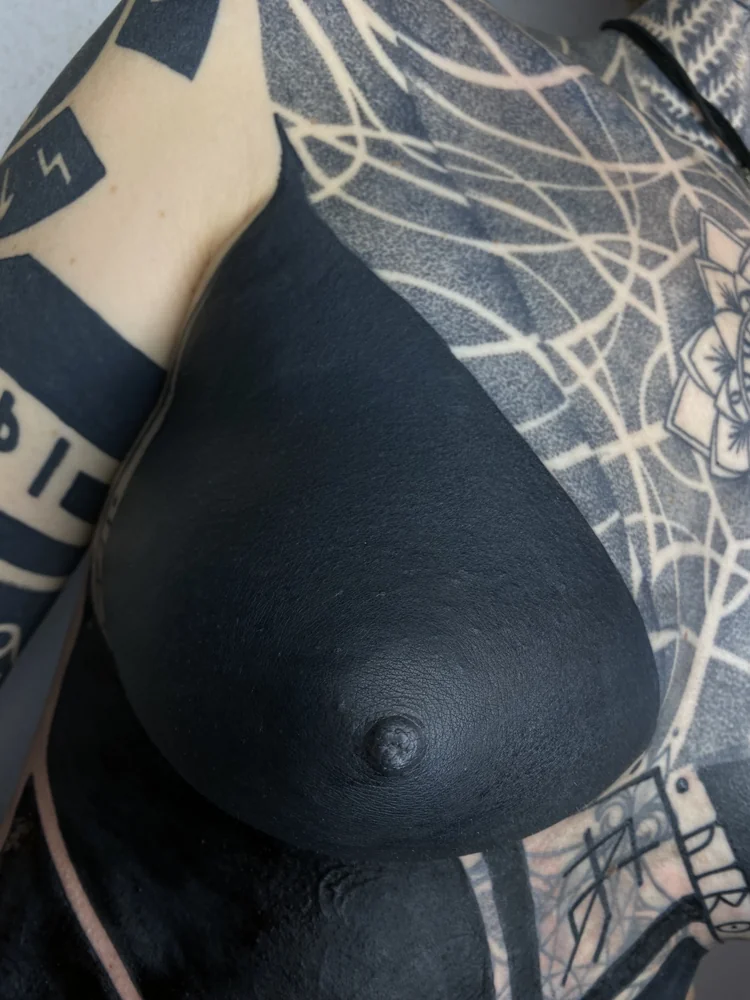 Abgeheiltes Blackout-Tattoo auf der Brust mit einer großflächigen schwarzen Form zwischen bestehenden Mustern, Detailansicht