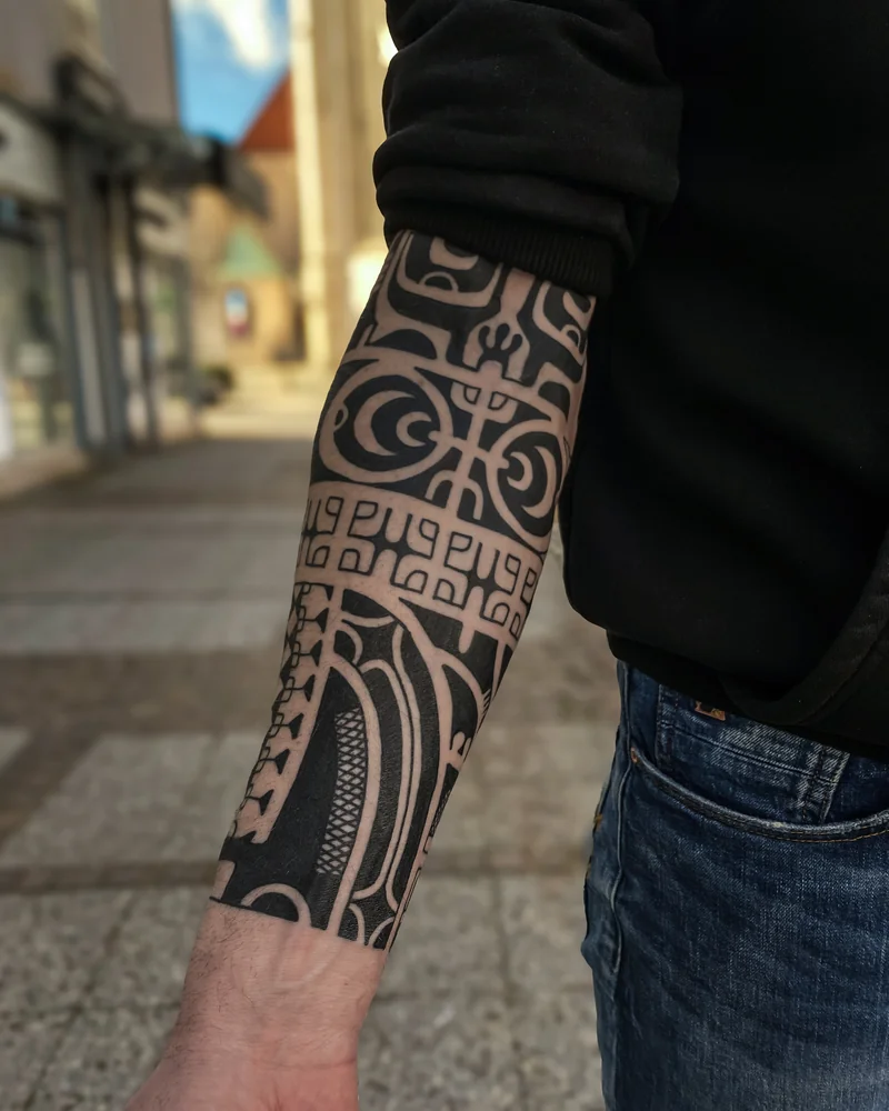 Marquesas-inspiriertes Unterarmtattoo mit figurativen Motiven, Musterbändern und schwarzen Flächen