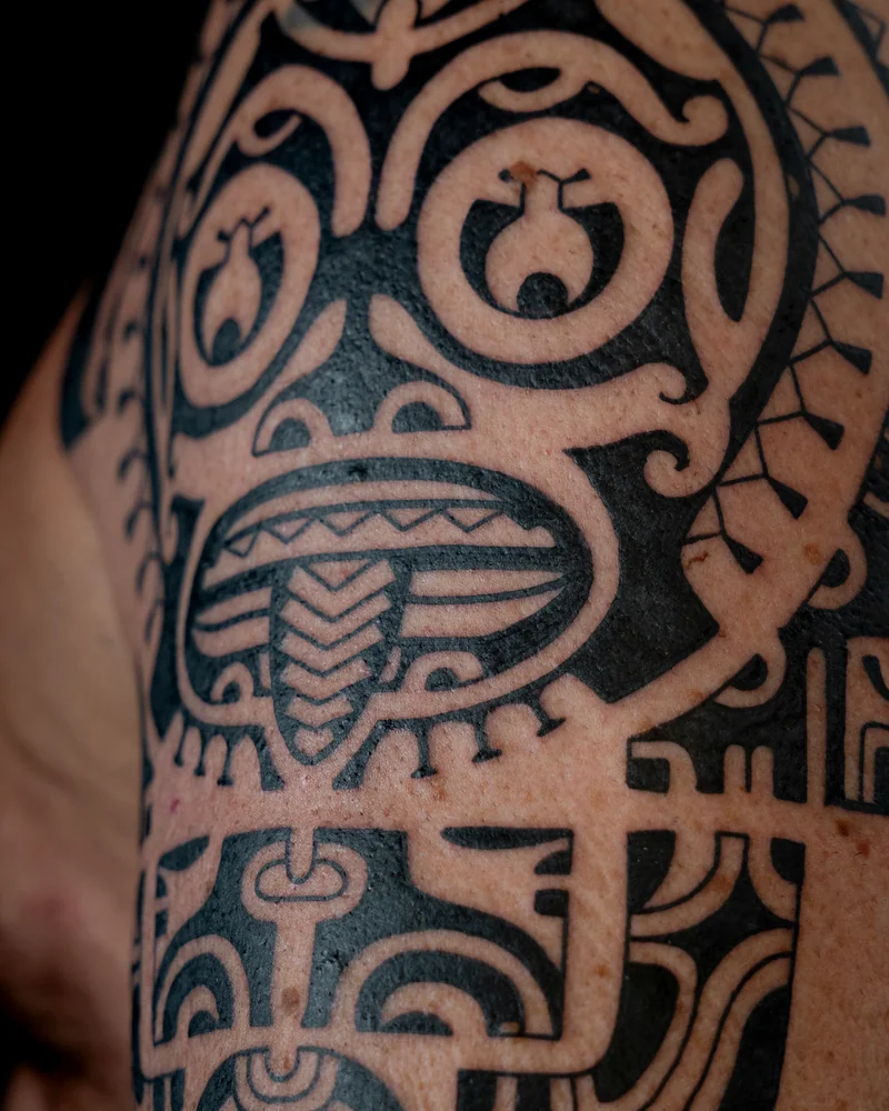 Detail eines Marquesas-inspirierten Tattoos mit figürlichen Motiven und schwarzen Linien