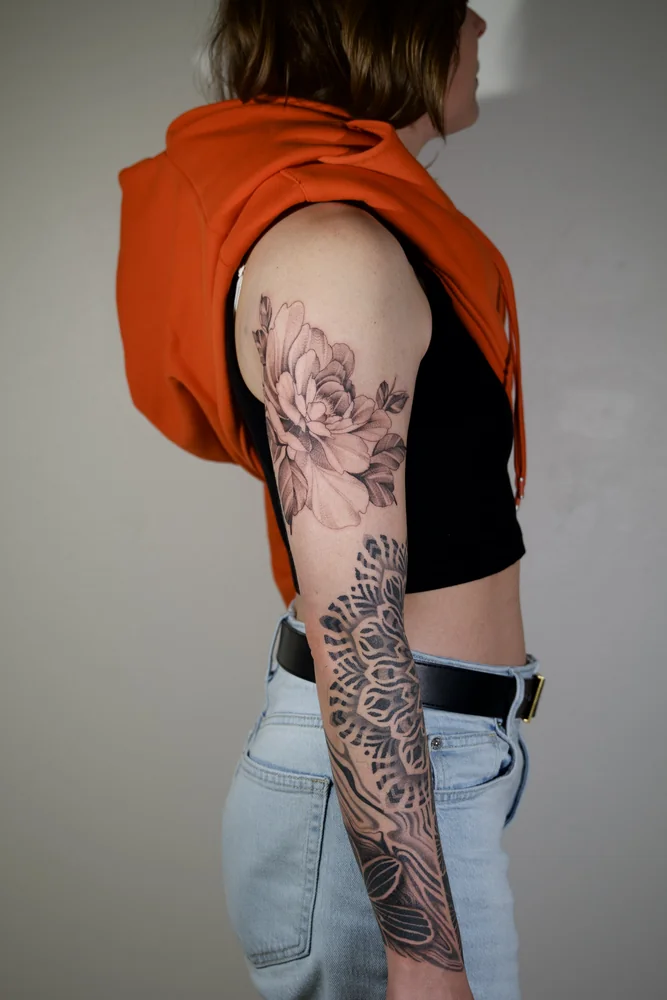 Florales Tattoo am Oberarm mit Blüten und Blättern sowie ornamentalen Mandala- und fließenden Mustern am Unterarm