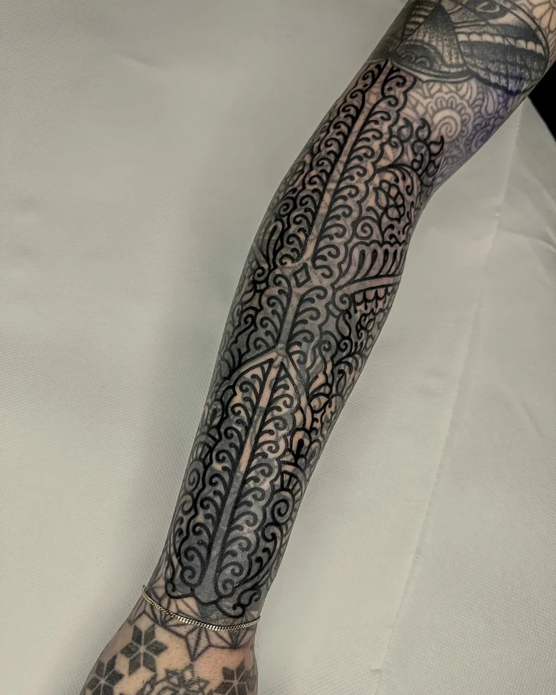 Dichtes ornamentales Tattoo am Unterarm mit geschwungenen Blättern und Bögen