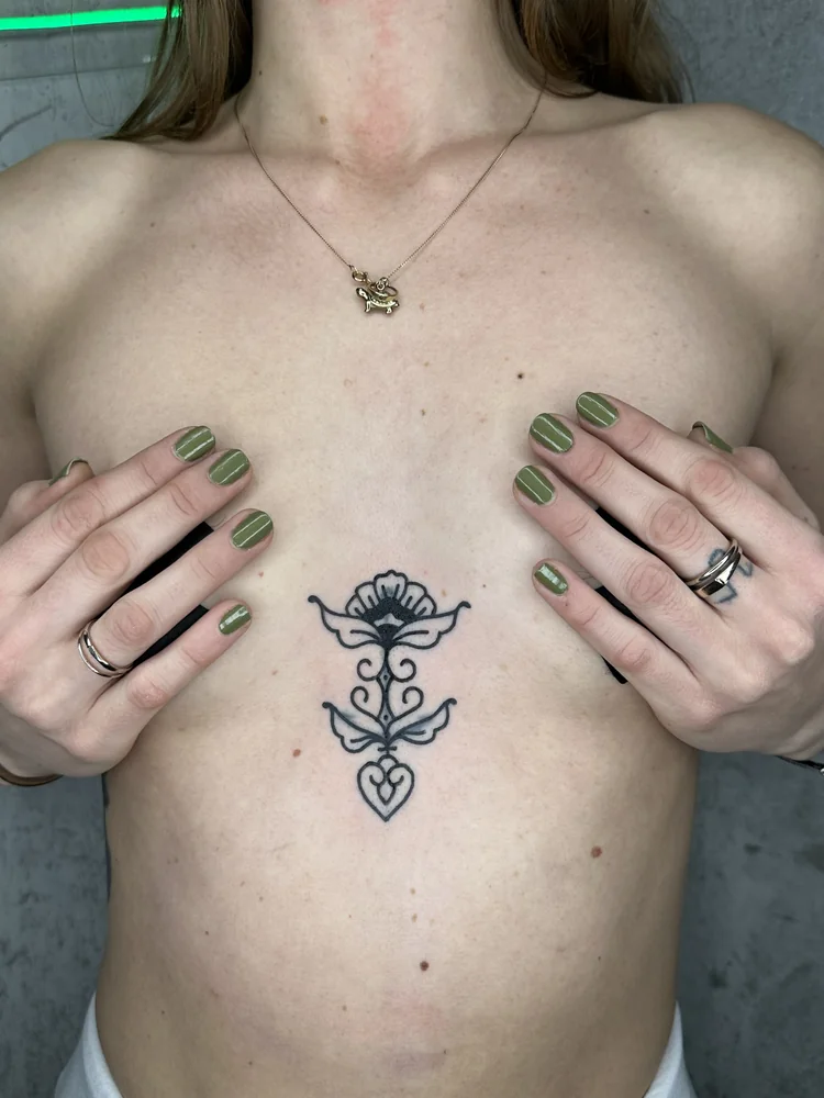 Frisch gestochen: Ornamentales Mini-Blast-over eines alten Tattoos am Brustbein mit einer Blüte, geschwungenen Blättern und einem Herzmotiv